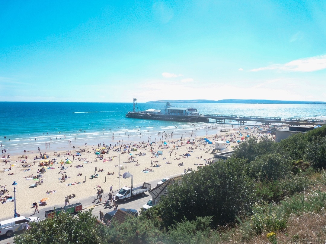 A relatively busy Bournemouth Beach under clear blue skies looking towards the Pier in the near-distance